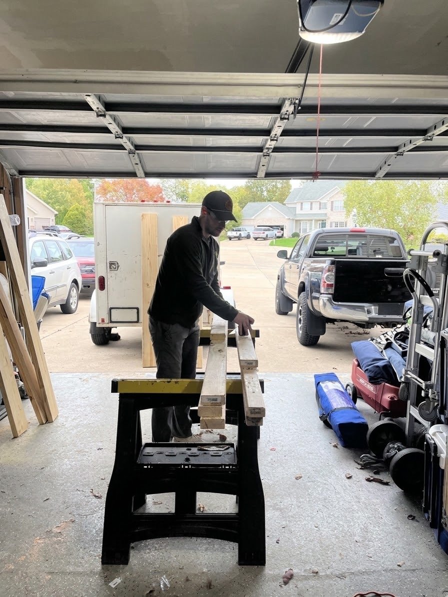 Dillon, owner of DAT Services, measuring lumber on a sawhorse in his garage workshop
